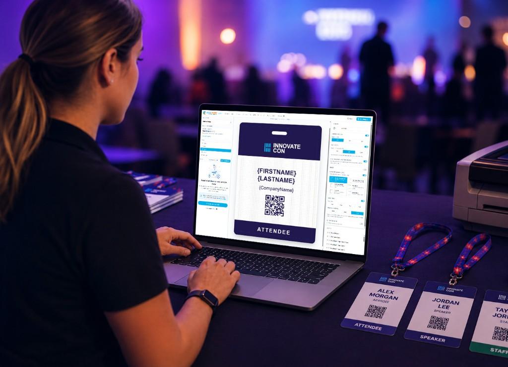 Event organizer designing attendee badges on a laptop with printed badges and a badge printer at a conference.